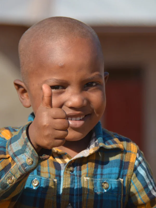 Tansanisches Waisenkind gibt den "Daumen hoch" und lächelt.